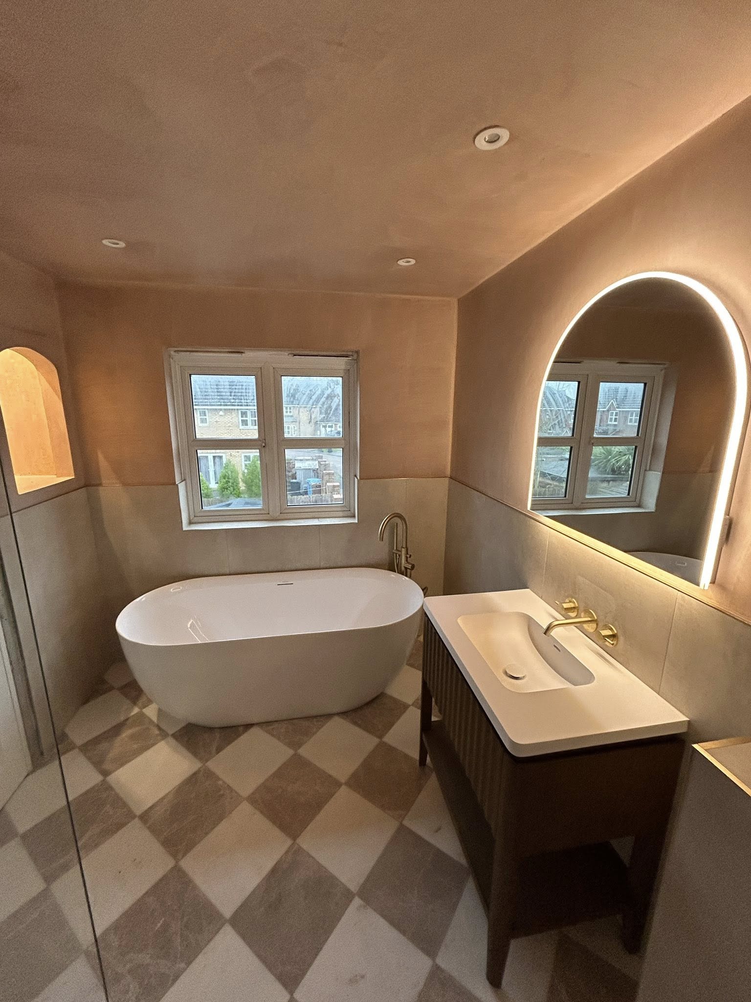 Bathroom with freestanding bath and arched backlit mirror